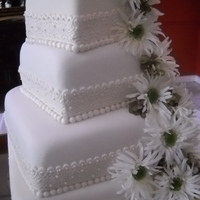 Maresa Slightly twisted on each other, this square design was embellished with a 'lace ribbon' and silk gerberas....