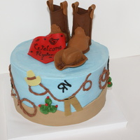 Western Shower Cake 8 inch round cake with blue buttercream icing. Fondant western theme decorations and gumpaste boots, cowboy hat, and bandana.