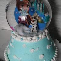 Frozen Snow Globe Strawberry cake in buttercream. The globe is glass, decorated with fondant snowflakes. The inside scene is a cut out of foam, paper plate...
