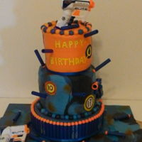 Nerf Cake For 3 Boys Fondant cake in nerf theme. The bottom tier is actual nerf bullets that can be used for a game of nerf war at the party.