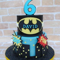 Batman Cake 2 tier batman themed cake covered in black and blue tinted chocolate ganache with fondant decor.